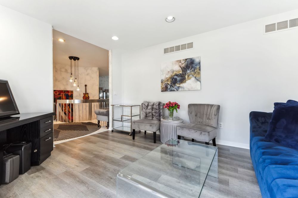 Modern living room with blue sofa, glass coffee table, light hardwood floors, and open layout.