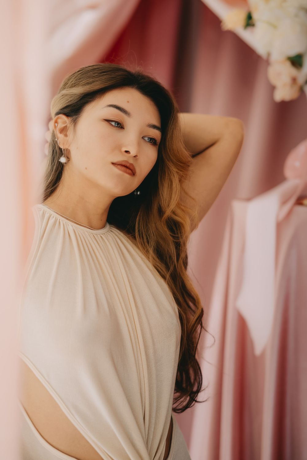 A woman in a white sleeveless top poses gracefully against a pink curtained backdrop in a series of elegant portraits.