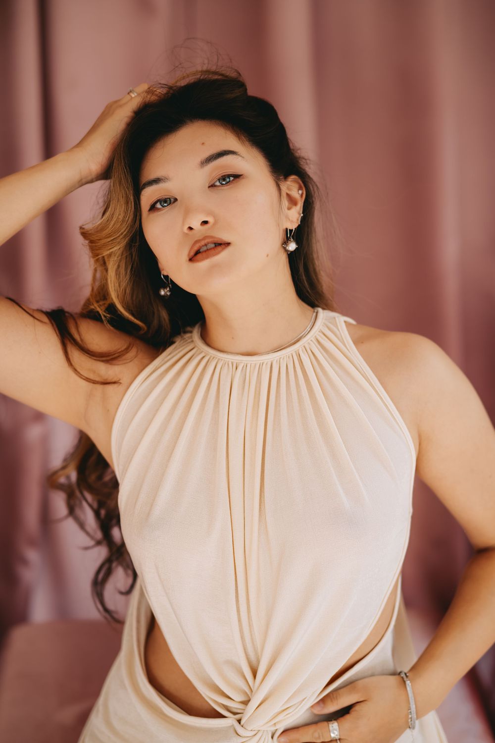 Woman in white sleeveless top poses against pink backdrop in glamour photoshoot series.