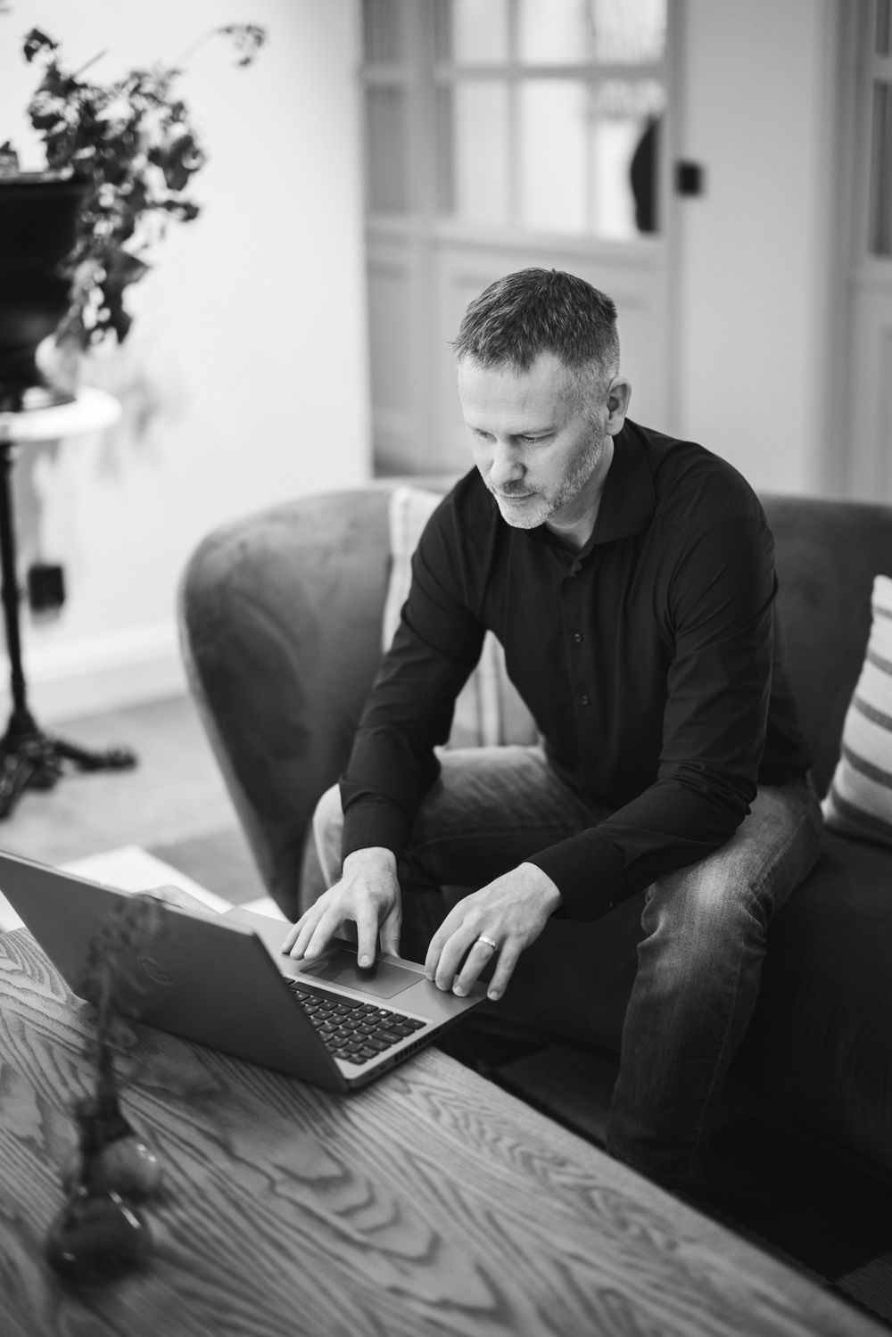 Professional working on laptop computer while sitting at wooden desk in monochrome office setting.