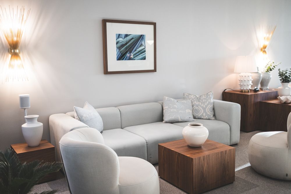 Modern spa treatment room with white massage table, wooden accent tables, and warm wall sconces creating a serene ambiance.