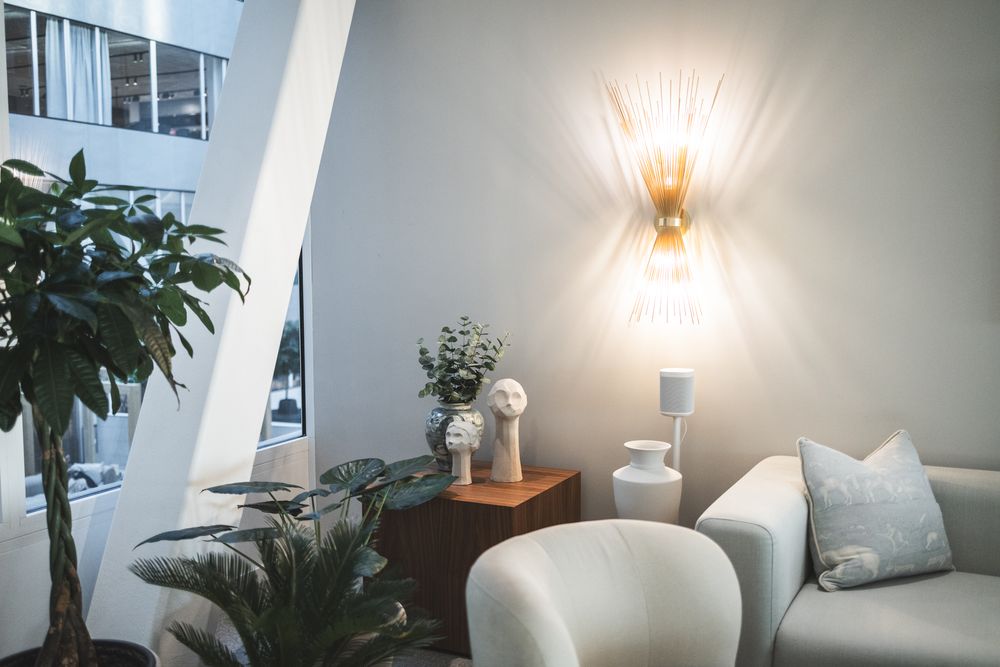 Modern minimalist living room interior with white walls, chandelier lighting, and potted plants by the window.