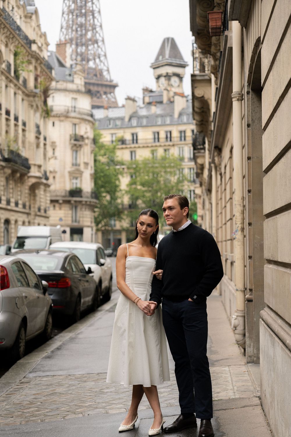 A Paris couple poses together on a romantic Parisian street with the Eiffel Tower. Paris cinematic photographer.
