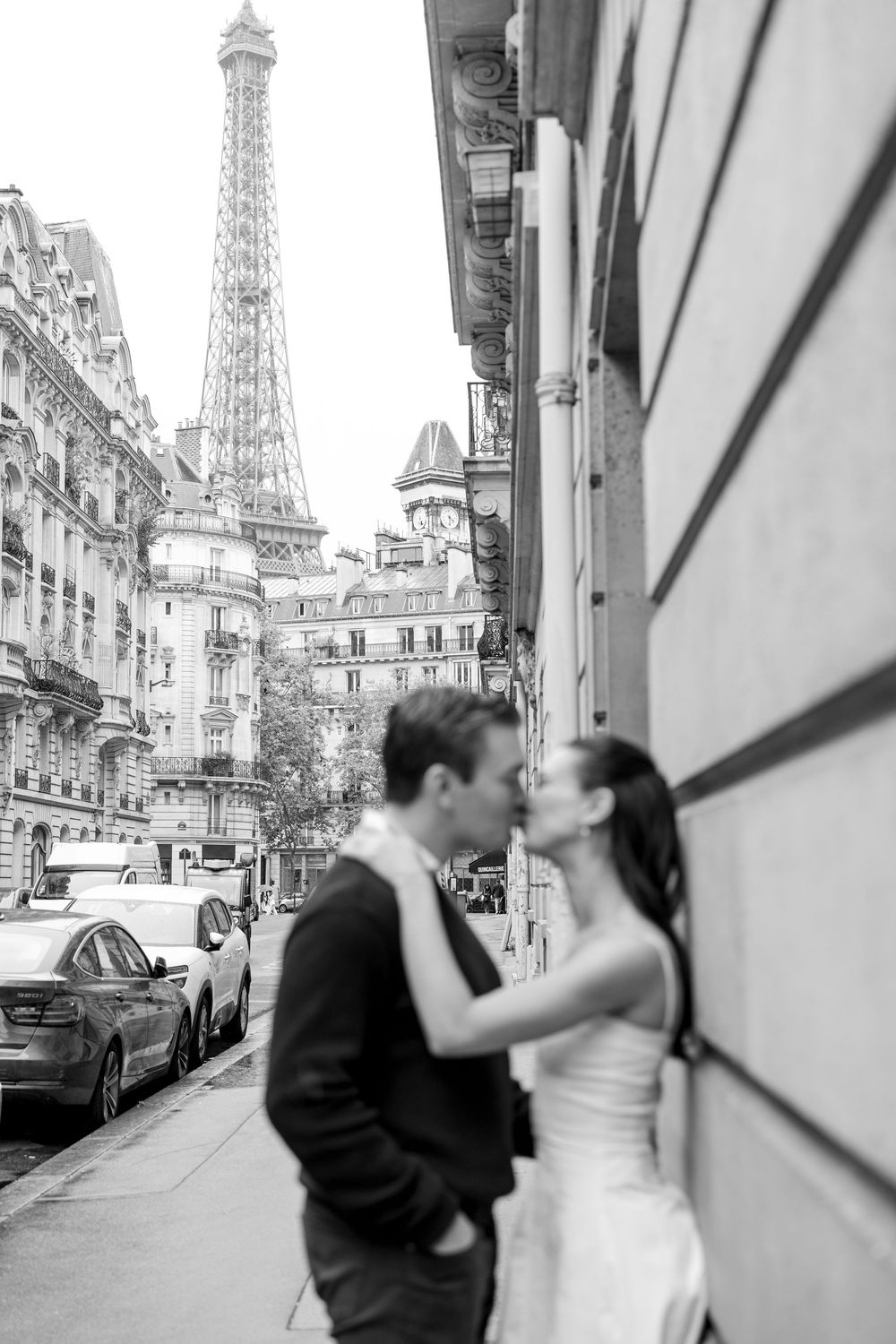 A romantic couple shares a kiss on a Paris street with the iconic Eiffel Tower visible in the background.
