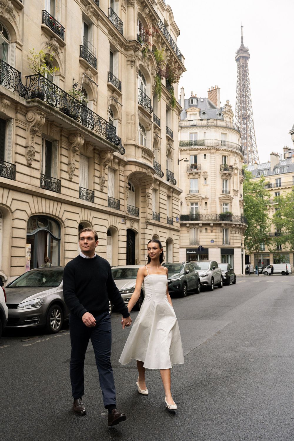 Paris couple walking playfully down a classic Parisian street with elegant Haussmann buildings. Cinematic Paris photographer. Cinematic.