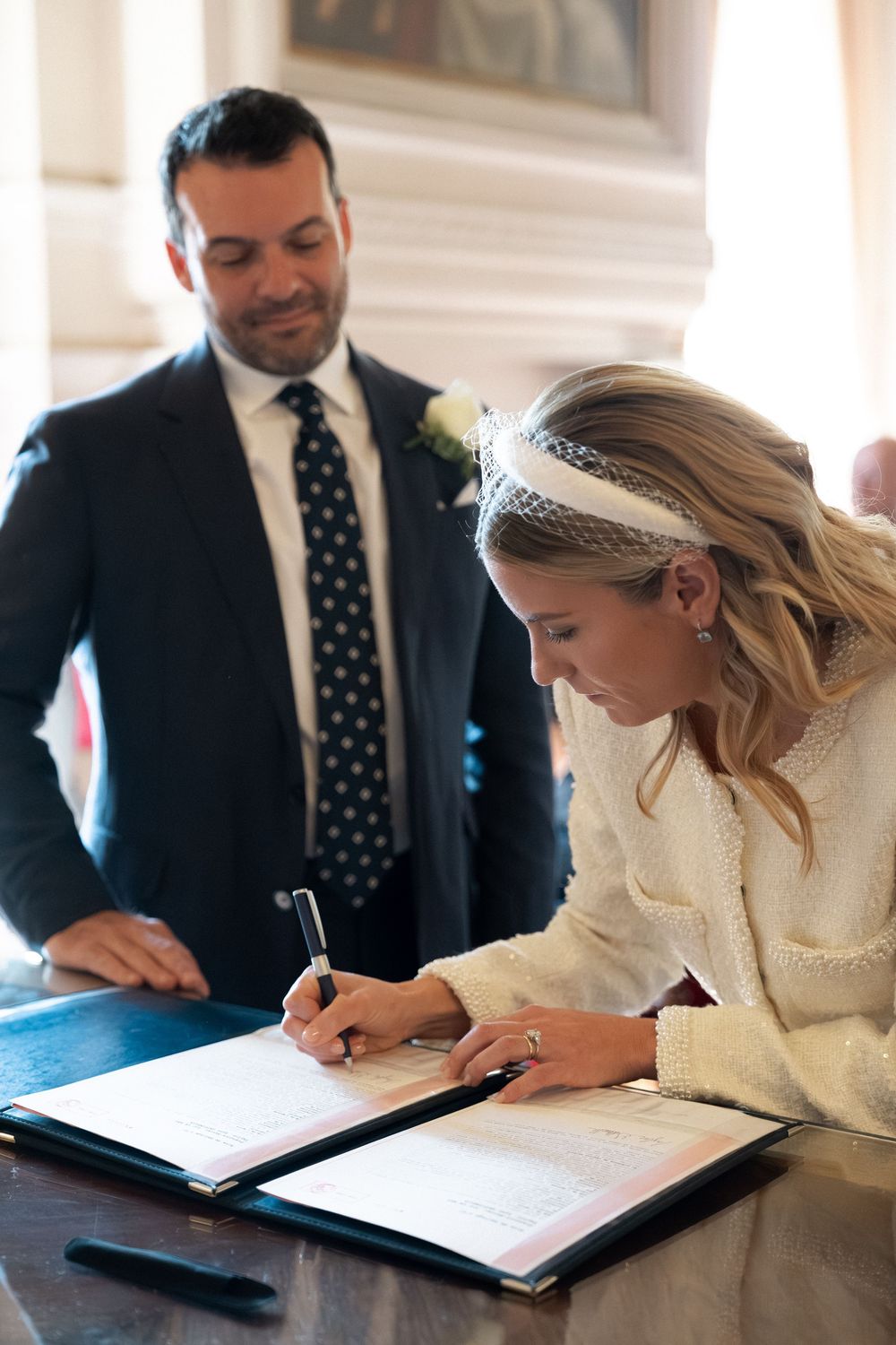 A sequence of photos showing a bride signing marriage documents at a table while wearing a white dress and headpiece. Paris civil ceremony.