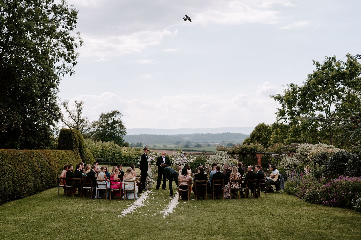 groom and wedding guests awaiting the brides entrance on the lawn, overlooking the black mountains at dewsall court in herefordshire