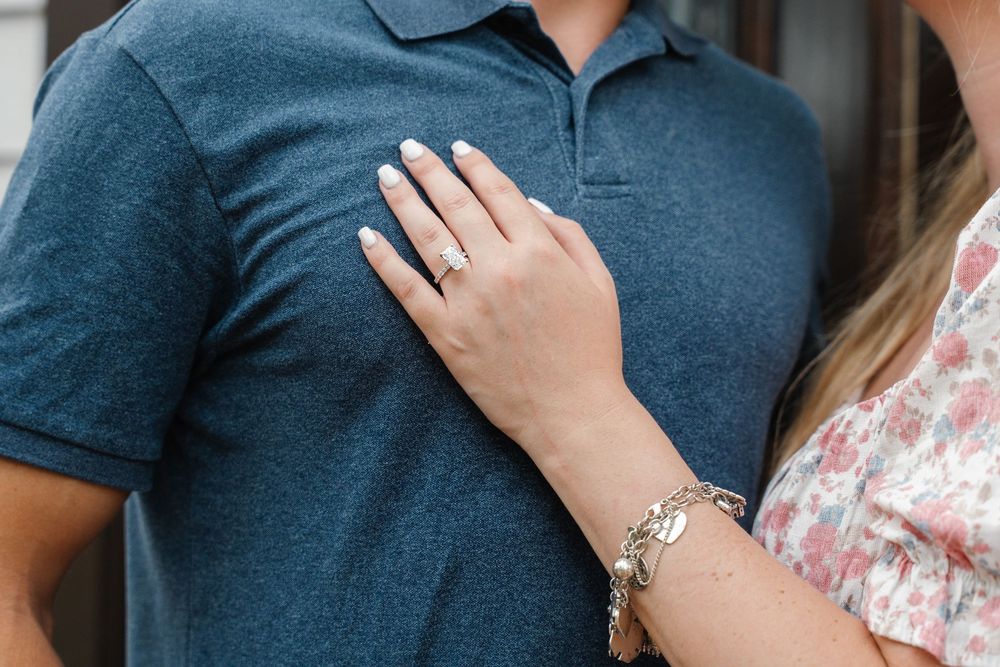 Close-up of woman showing engagement ring and gold bracelet with hand resting on mans blue polo shirt.