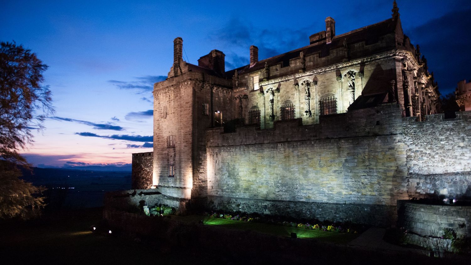 Stirling Castle walls lit up at dusk with dramatic blue sky.