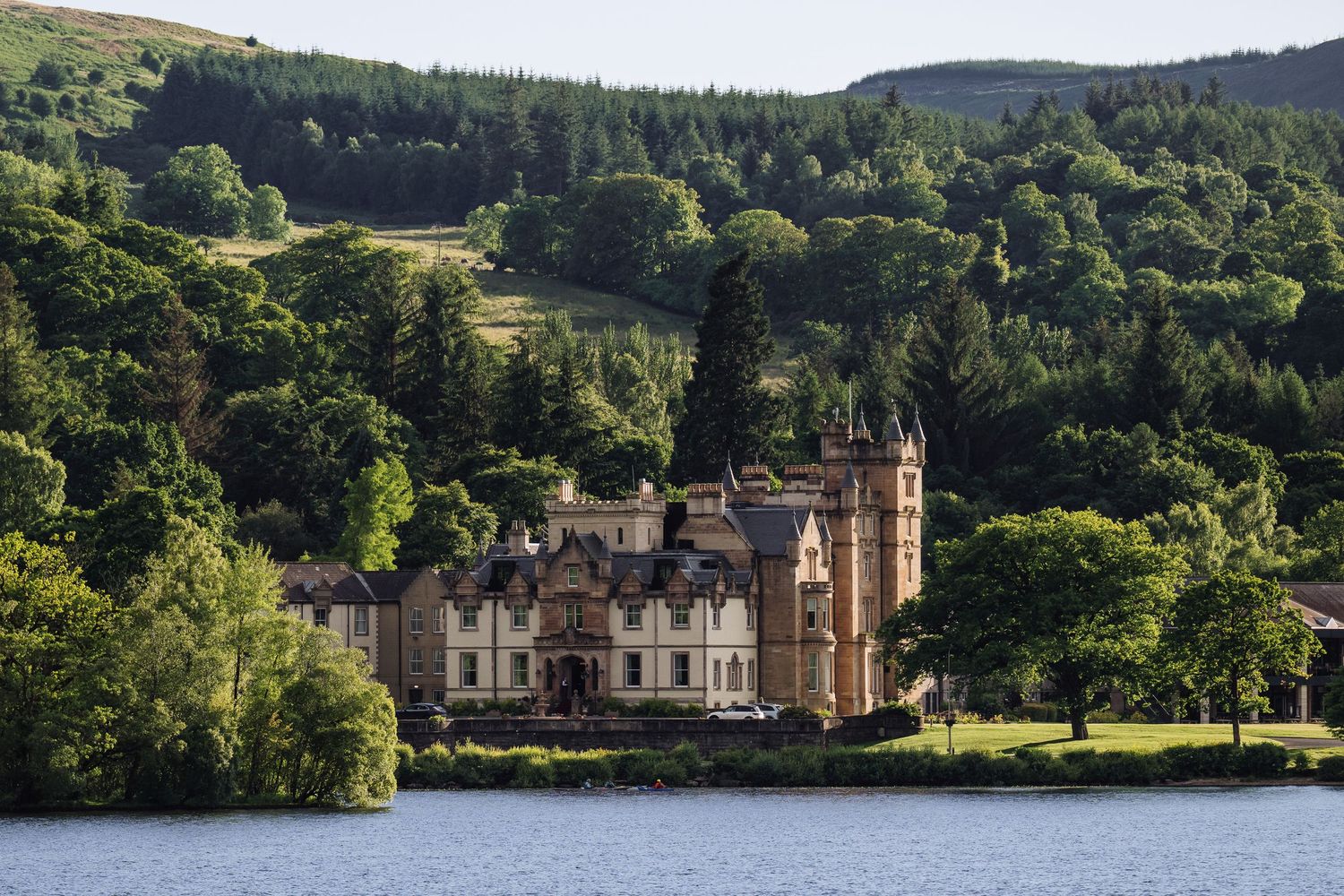 Scenic lakeside view of Cameron House nestled among green hills and forests.