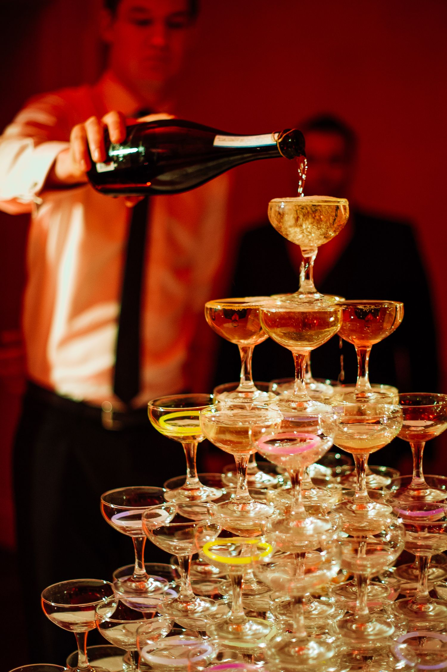 Champagne being poured into a tower of coupe glasses stacked in an elegant pyramid formation.