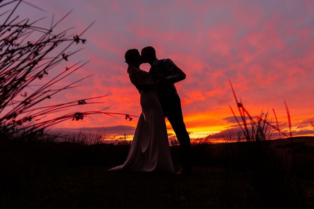 Silhouettes of figures standing in a field during a vibrant red sunset. Woodhill Hall.