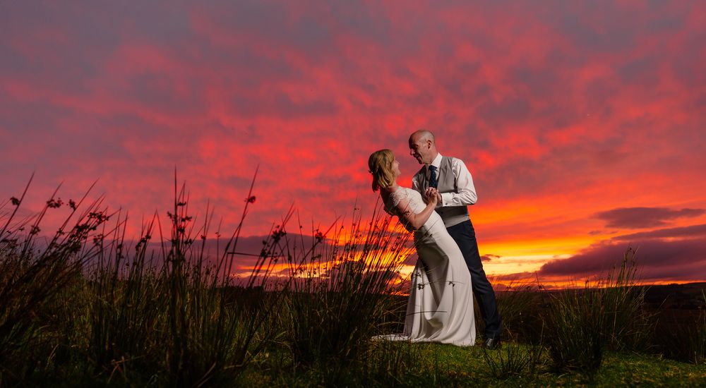 Silhouettes of a couple embracing against a dramatic red and orange sunset sky. Woodhill Hall.