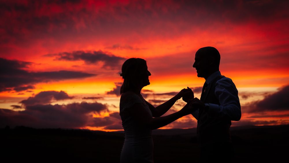 Dramatic sunset silhouettes create a romantic wedding portrait against vibrant orange and red skies. Woodhill Hall.