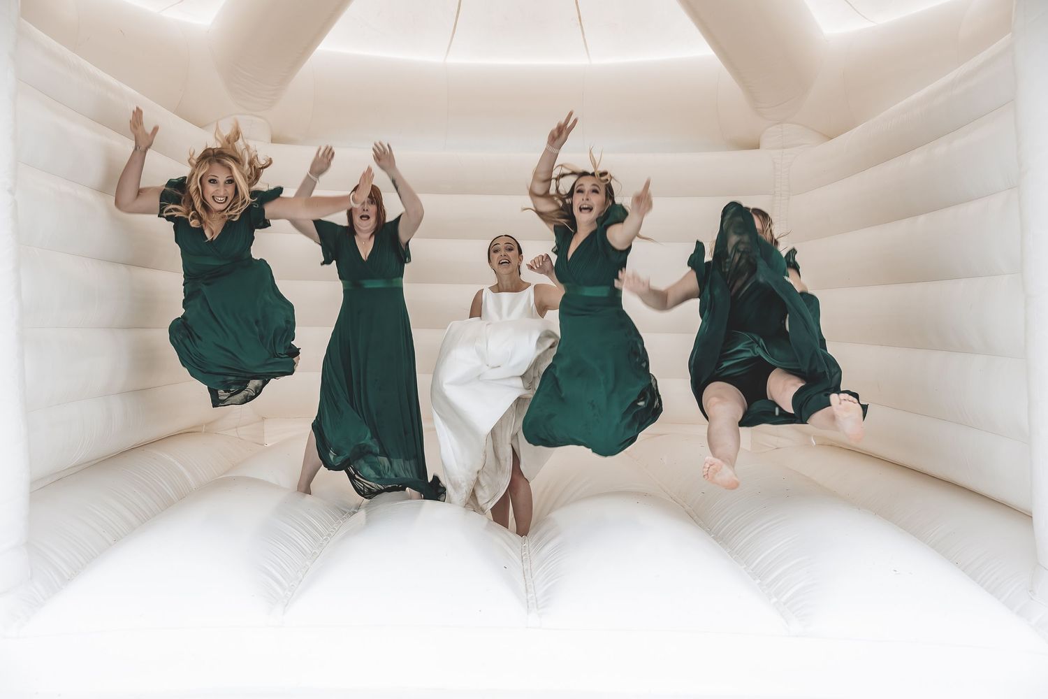 A documentary wedding image of a bride and bridesmaid enjoying a fun moment on a bouncy castle during their rainy wedding day.