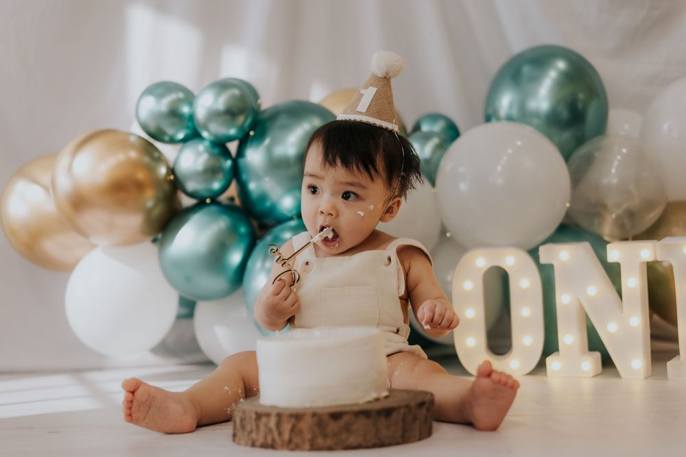First birthday party decorations with teal and white balloons and gold 'ONE' text sign displayed on wooden surface.