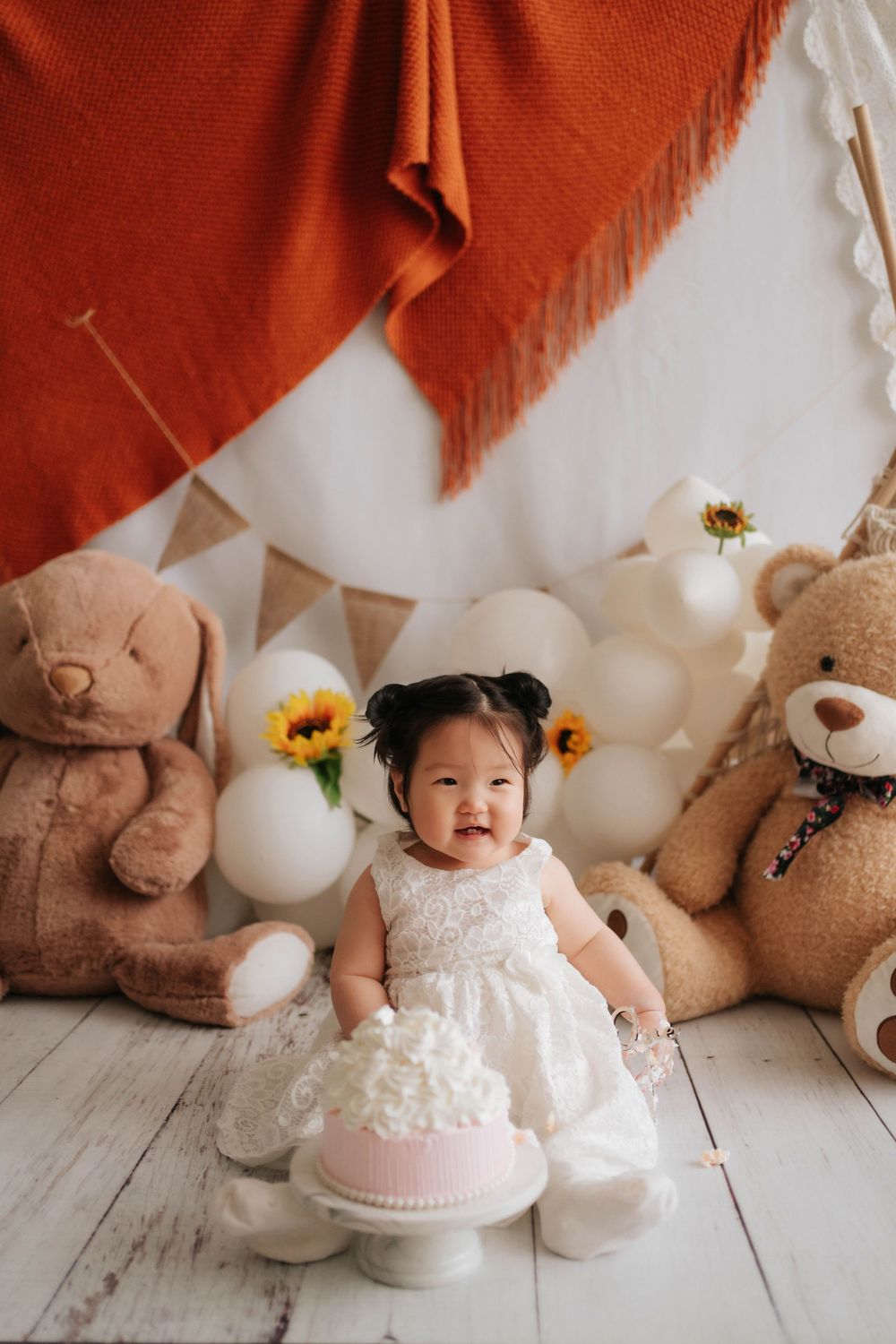 Sequence of cake smash photos showing a baby in white dress with teddy bears, balloons and pink drapes in background.