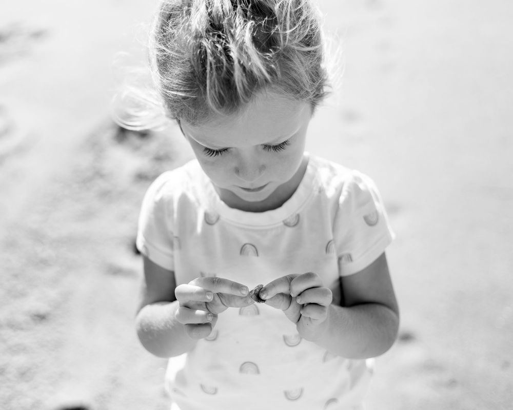 A black and white photo showing a small child playing in sand at the beach.