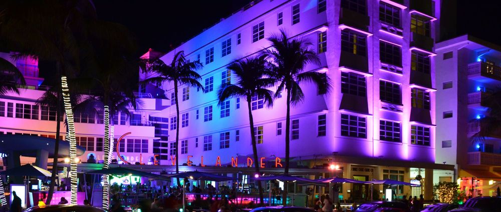 The Clevelander Hotel glows with bold neon colors—purple, pink, and blue—surrounded by palm trees wrapped in lights.