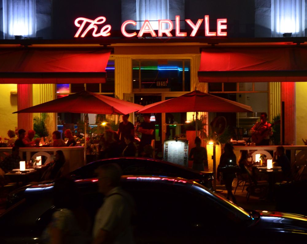 The Carlyle glows with bold red neon lighting as diners fill the outdoor tables beneath vibrant umbrellas.