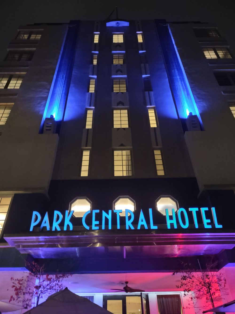 The Park Central Hotel glows in vibrant blue and purple neon lighting, highlighting its classic Art Deco lines and symmetrical façade.