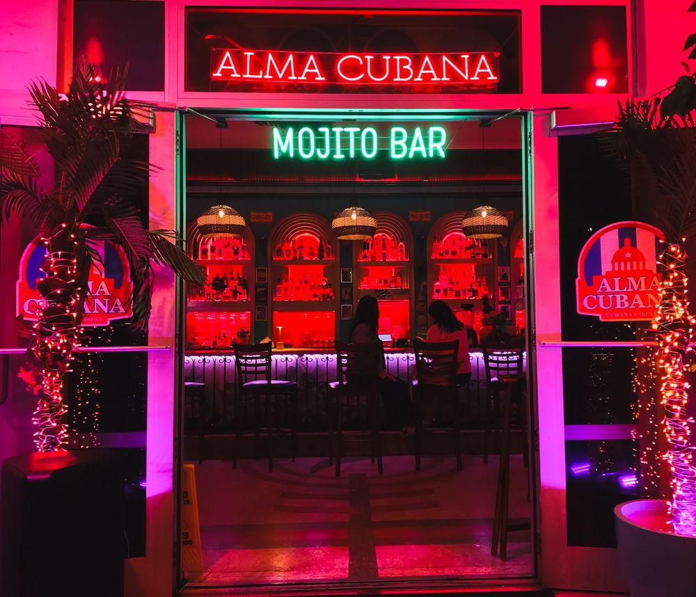 A glowing Cuban‑themed bar with red and green neon signage invites guests into a warm, tropical atmosphere.