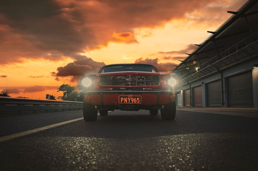 Silhouette of a classic Mustang against a dramatic orange sunset sky.