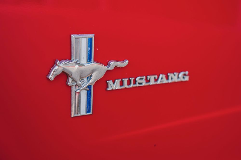 Chrome Mustang emblem and badges on a classic red Ford Mustang exterior.