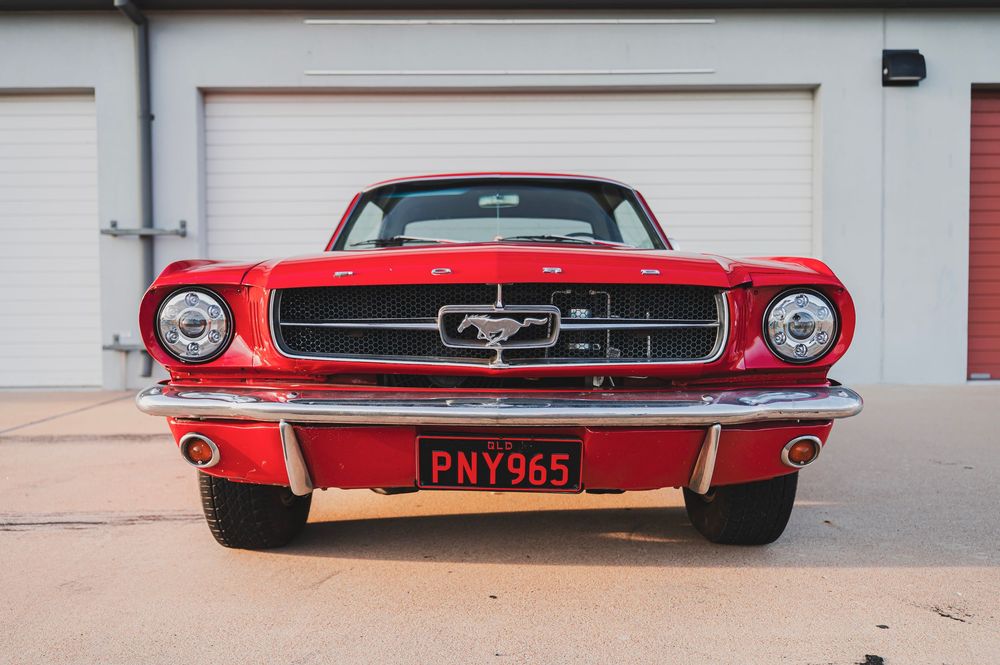 Front view of a classic red Ford Mustang showcasing its iconic grille and headlights against a white garage door.