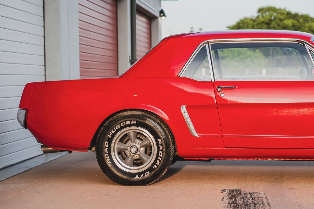Classic red Ford Mustang showcasing its sleek side profile and chrome details against a garage backdrop.