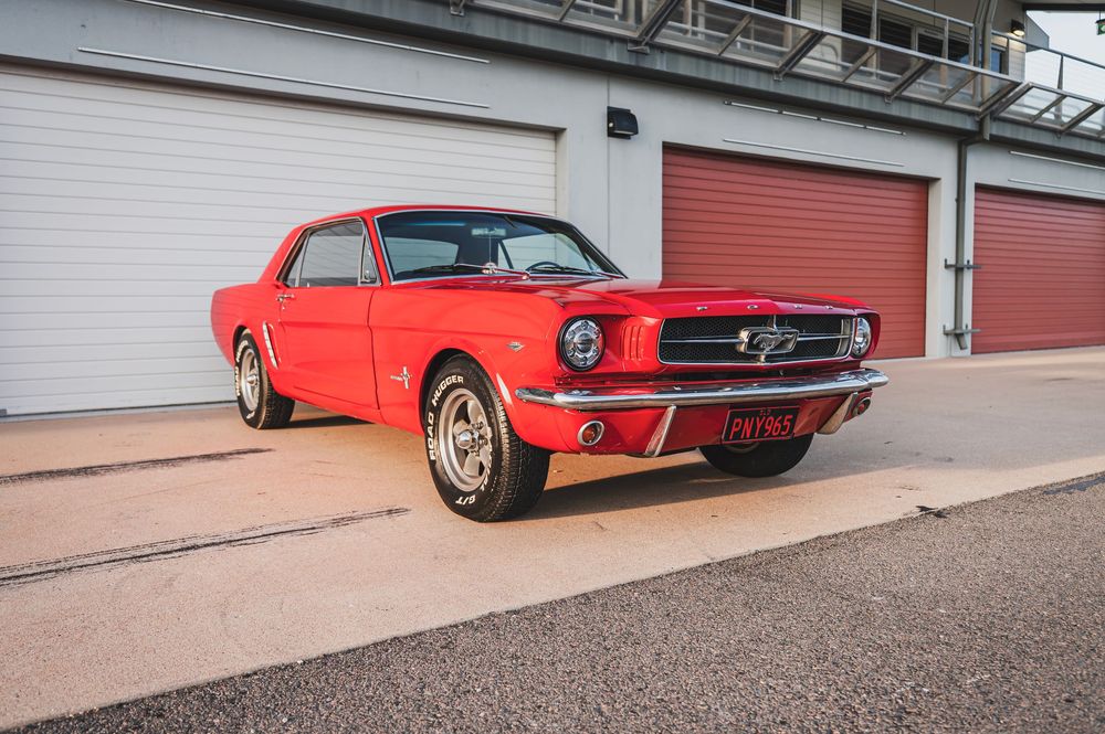 Low angle view of a classic red Mustang showing its sleek profile against a modern building exterior.