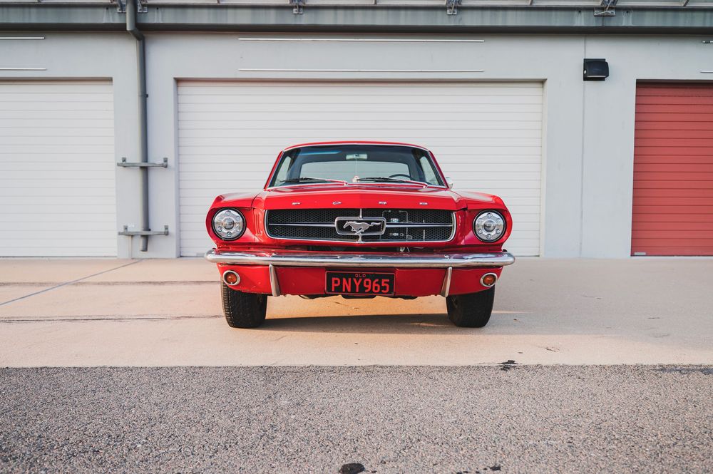 Classic red Ford Mustang parked in front of storage units with white doors and red trim.