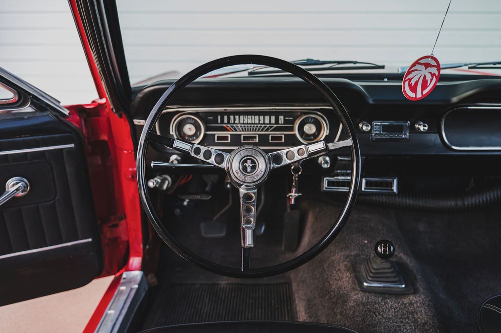 Vintage black dashboard and steering wheel interior of a classic Ford Mustang.