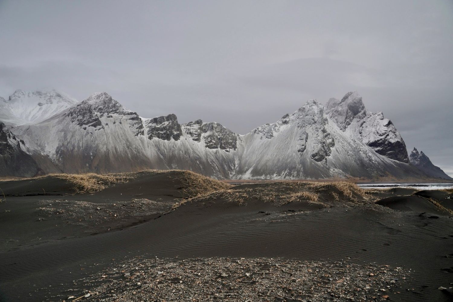 Panoramic view of snow-capped mountain peaks with dramatic clouds and rugged terrain in the foreground.