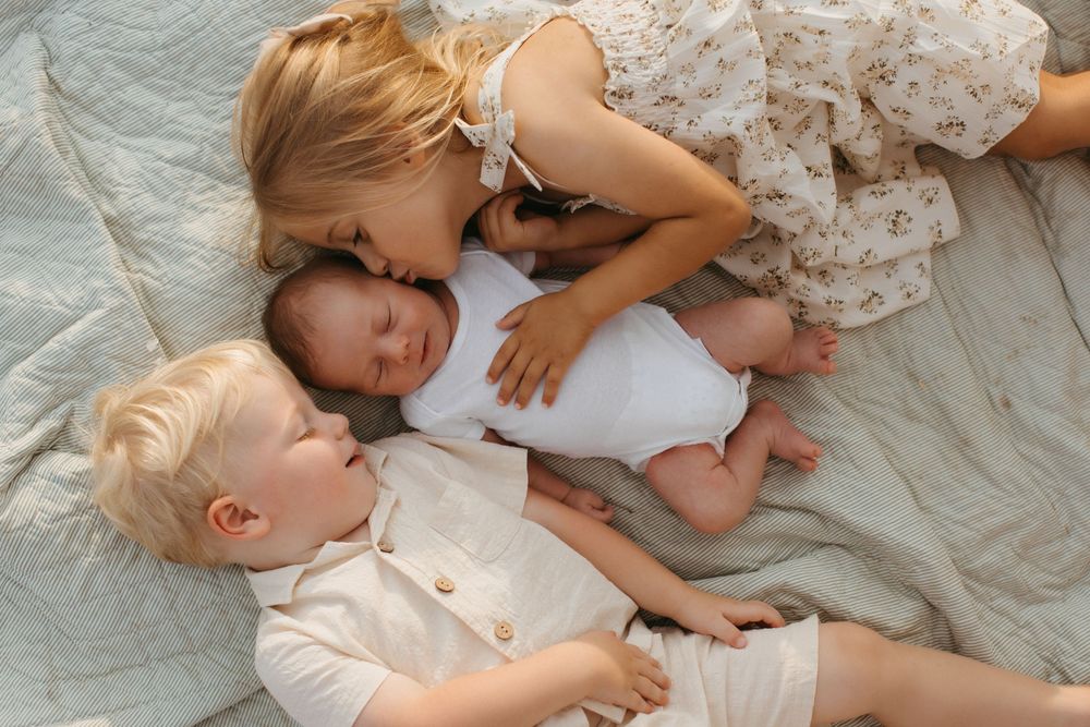 Three children lay close together on light colored bedding in a sweet, intimate moment.