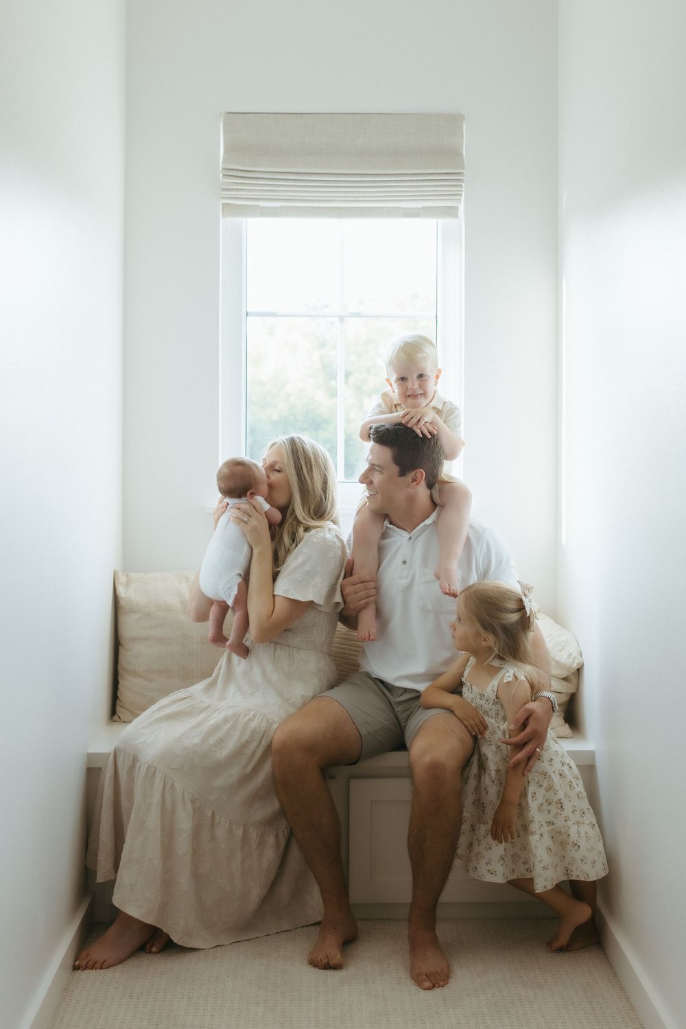 A family shares a tender moment together while sitting on a window seat in a bright, airy space.