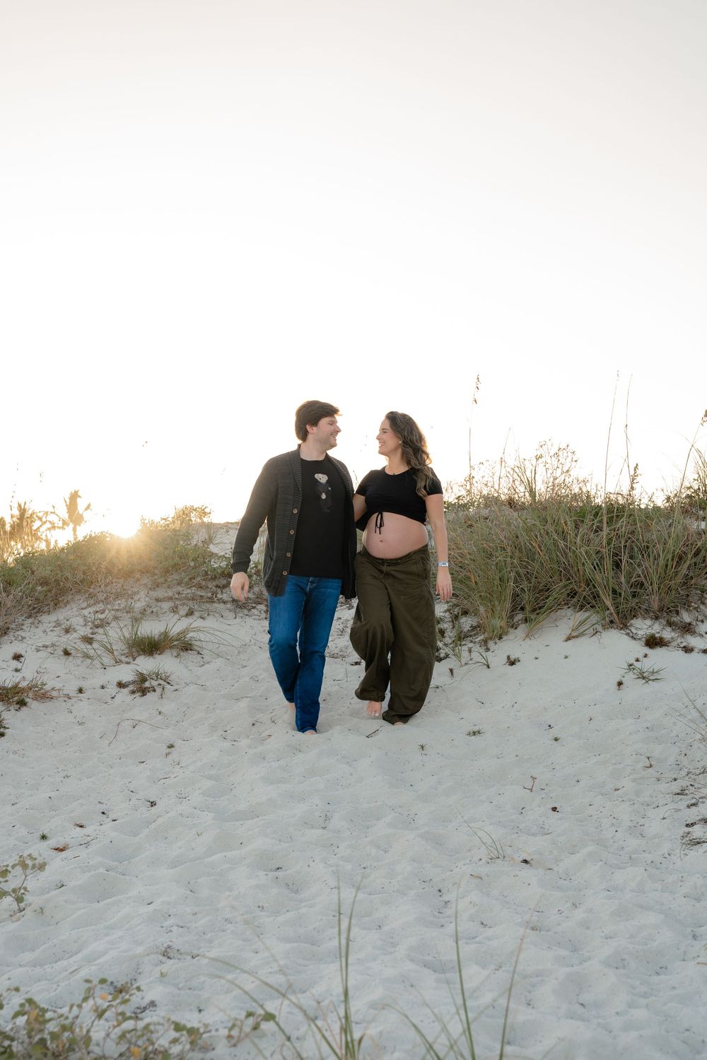 Couple walking along white sand dunes during sunset with beach grass in background.