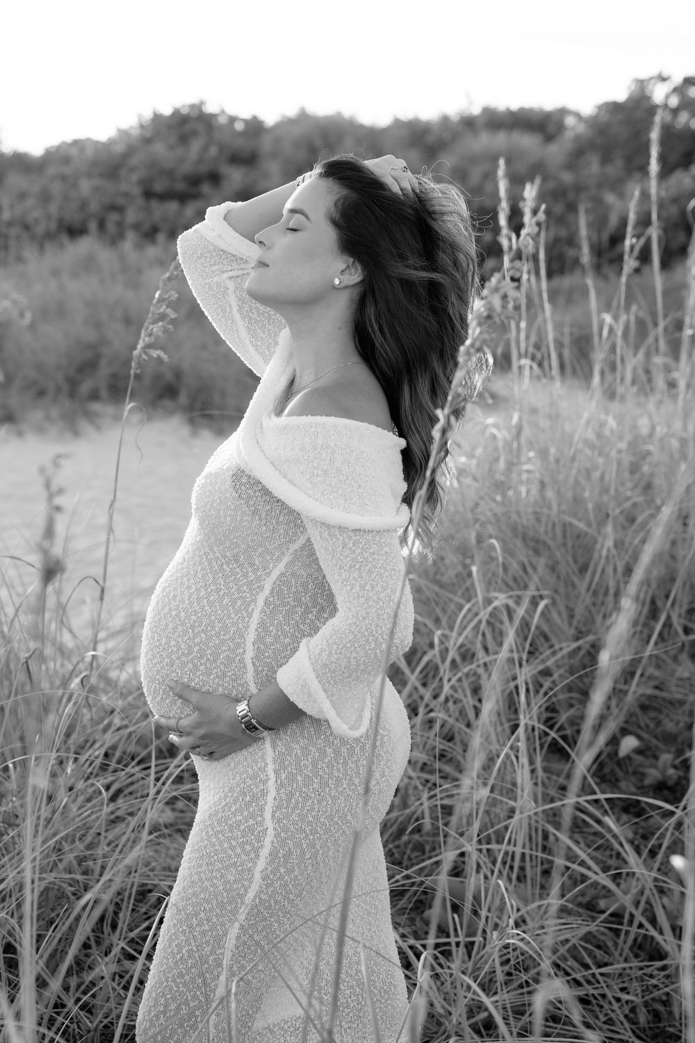 Artistic black and white portrait series in tall grass showing ethereal poses in a dotted dress at sunset.