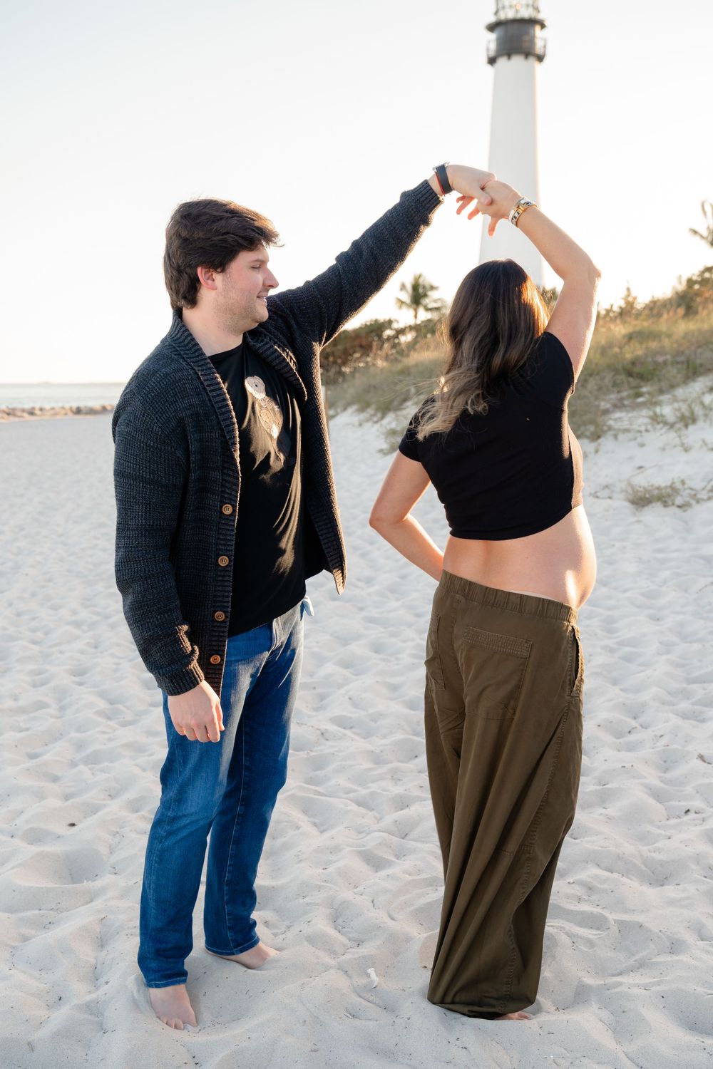 A couple poses playfully on a sandy beach at sunset, creating silhouettes against the dunes.