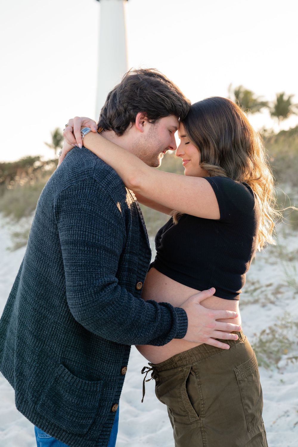 Intimate embrace captured against white sandy beach backdrop during golden hour.