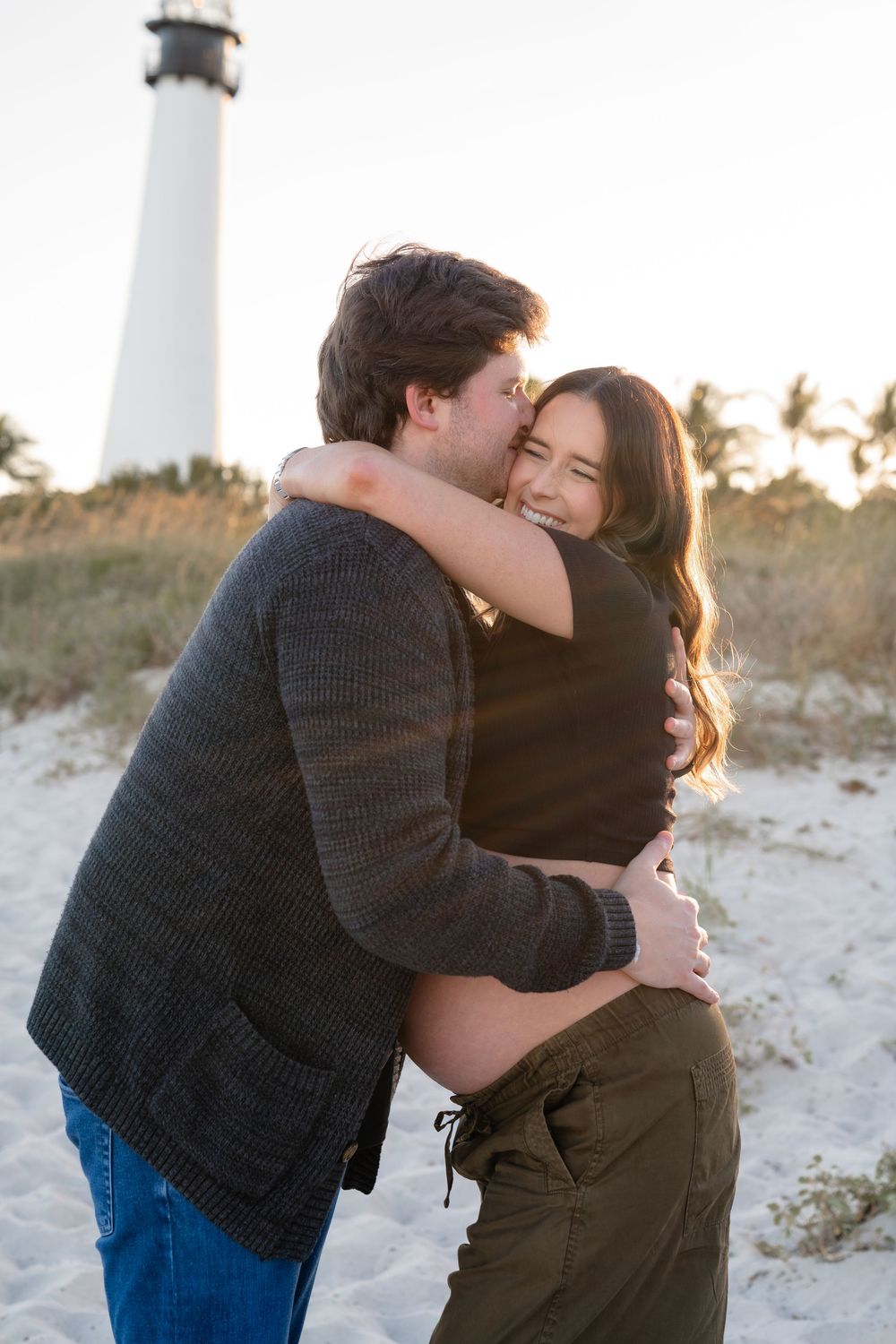 A couple embraces and shares romantic moments together on a sandy beach at sunset.