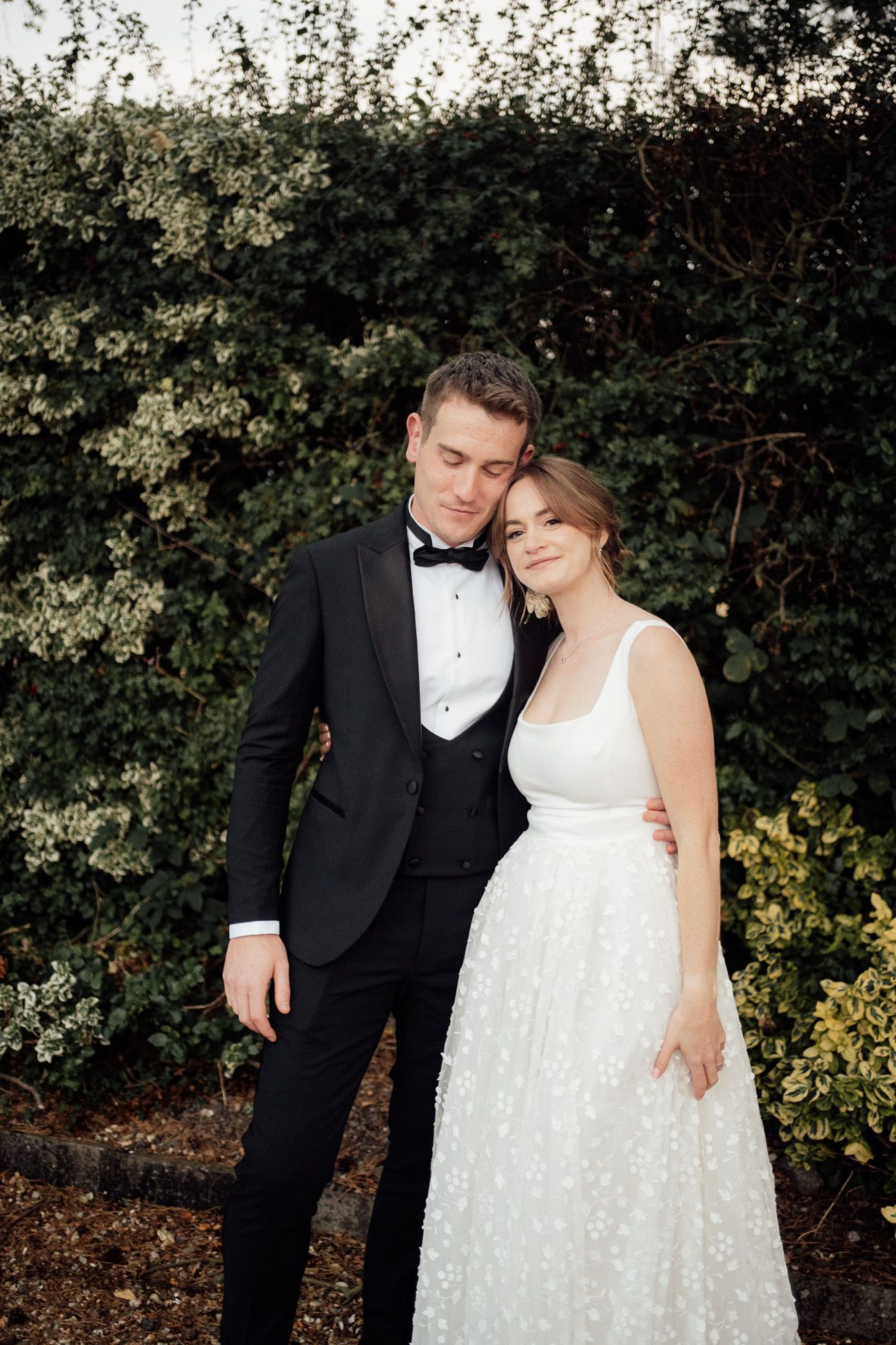 A romantic wedding couple poses together outdoors against a backdrop of lush green foliage and hedges  at Larkspur Lodge venue