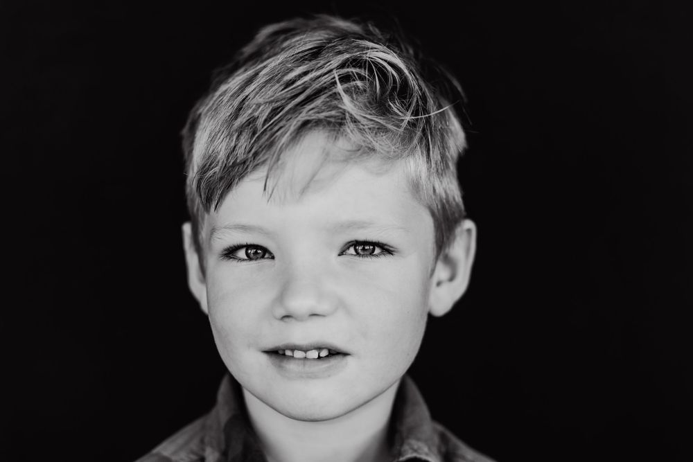 Black and white fine art portrait of a little boy looking at the camera with sad eyes part of school portrait.