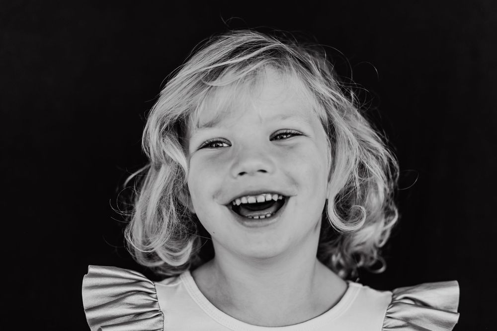 Black and white portrait of a little girl with blond hair laughing and looking strait but not to the camera.
