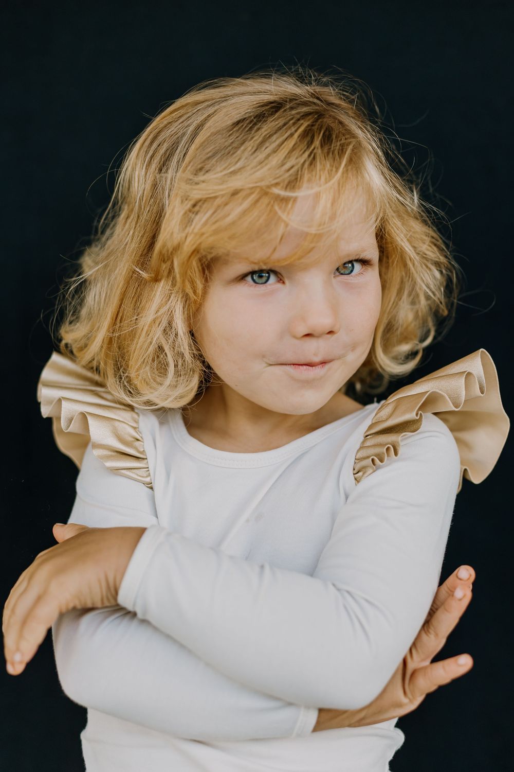 Photo of a girl with white shirt on black background with cross hands looking to her left side as part of school portrait session.