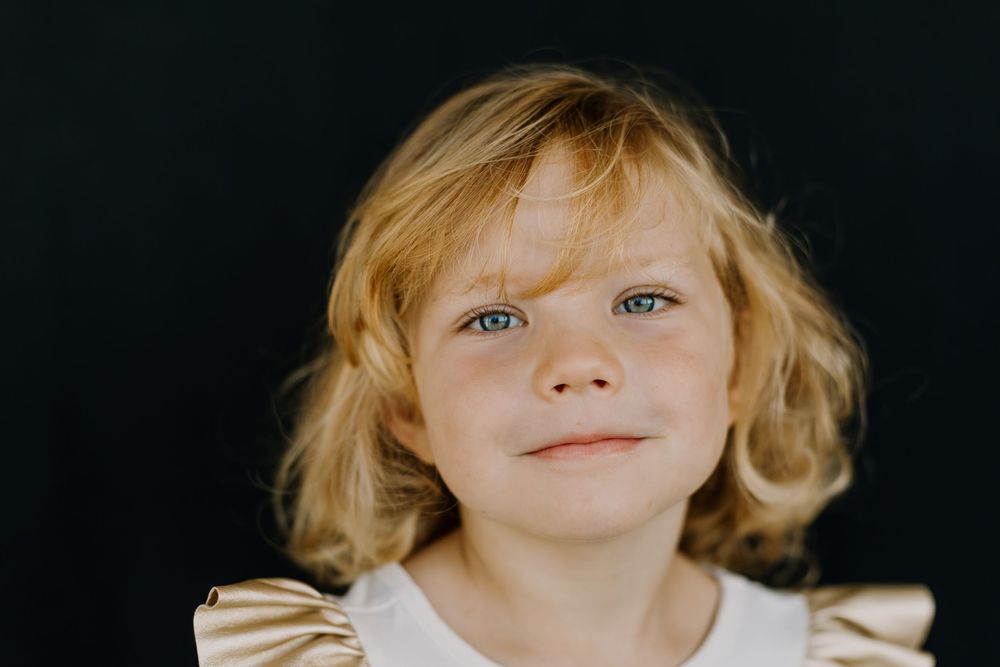 Photo of a blond girl with white shirt on black background  looking at the camera part of school photoshoot.