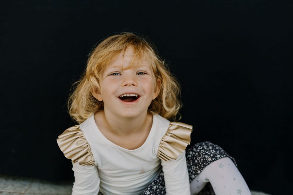 Portrait of a blond girl sitting and laughing while looking at the camera as part of school fine art session.
