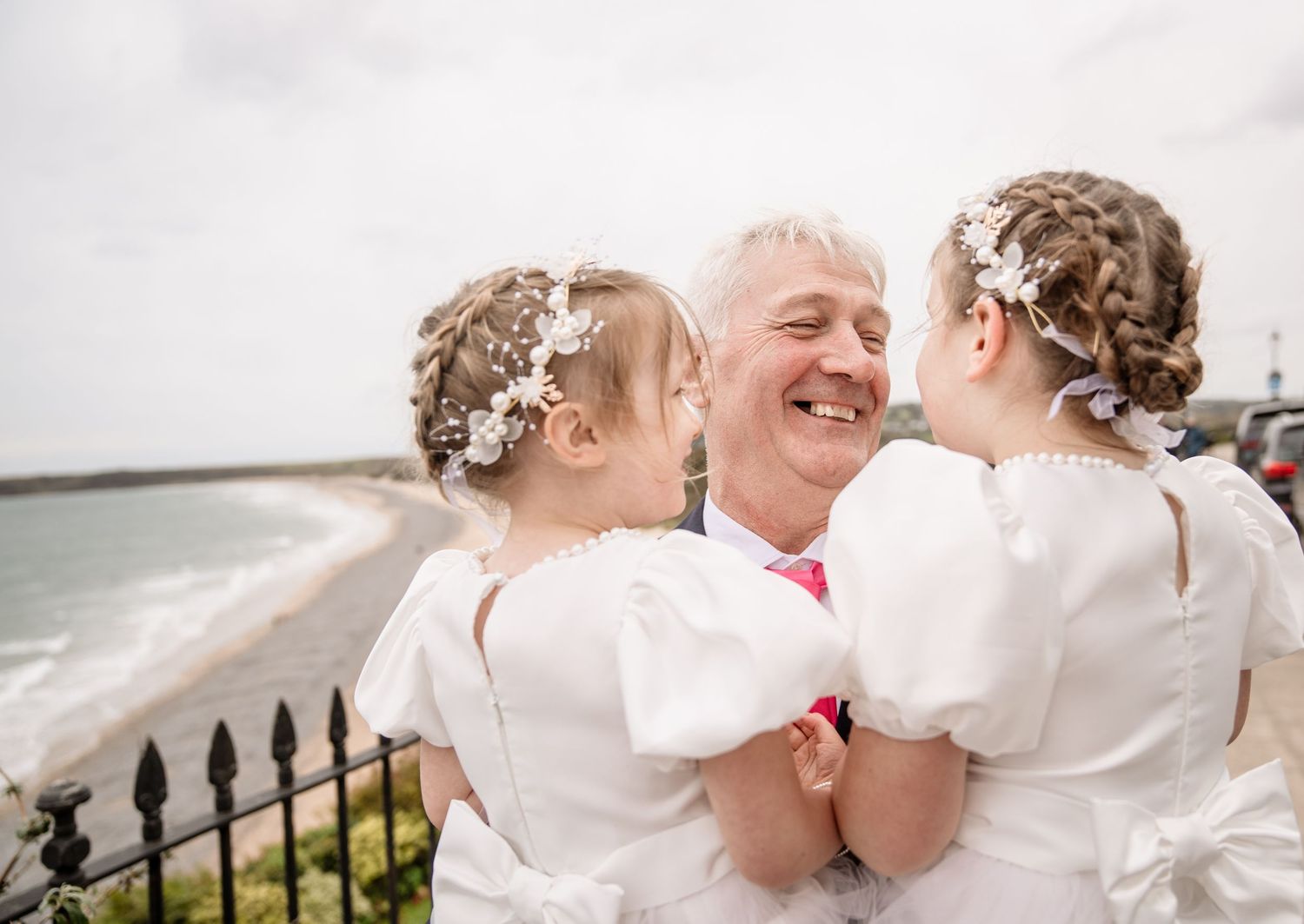A joyful moment shared between loved ones wearing white outfits with floral hair accessories by the seaside.