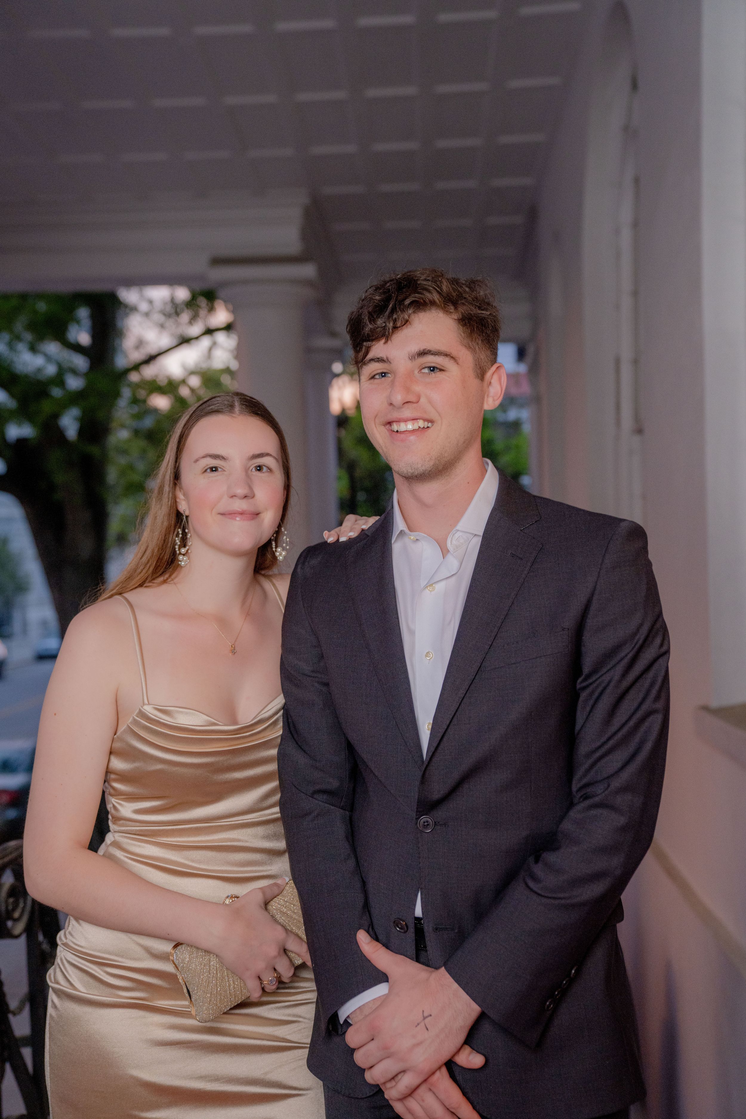 A couple poses together at a formal event, with one wearing a champagne silk dress and the other in a dark suit.
