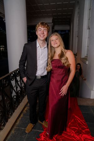 A couple in formal attire poses together in a hallway with white columns and decorative railings.